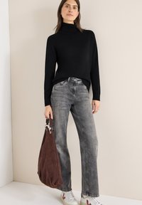 Černý rolák, šedé rozšířené džíny, hnědá semišová taška se stříbrnými kovovými doplňky a bílé tenisky s barevnými detaily.