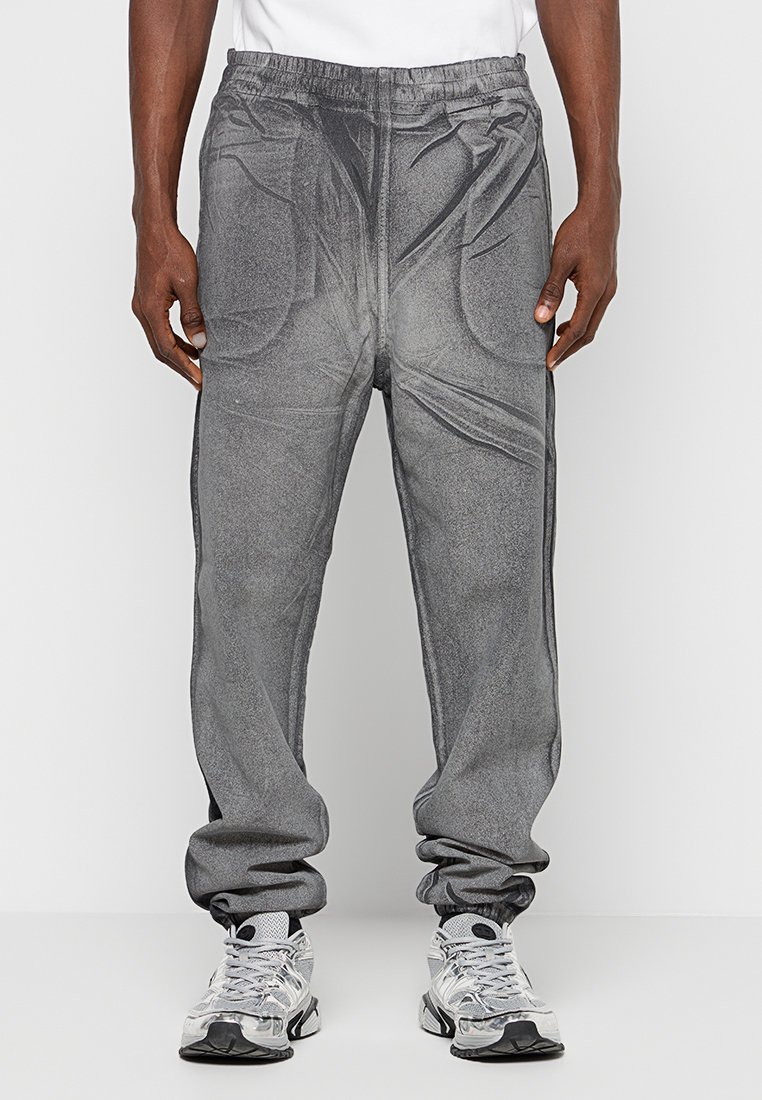 Graue Jogginghosen mit strukturiertem Finish, elastischem Bund und seitlichen Taschen. Am Knöchel schmal zulaufend, kombiniert mit silbernen Sneakers.