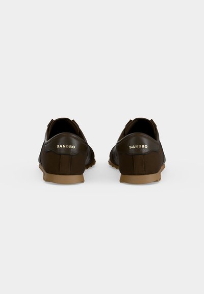 Paire de baskets en cuir marron foncé à coupe basse avec des semelles en caoutchouc beige, vues de dos montrant le logo "SANDRO" sur chaque talon.