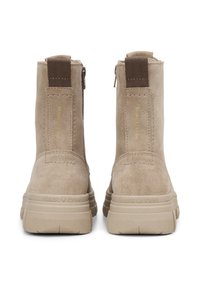 Bottines beiges en suède avec une surface texturée, une fermeture éclair et une semelle en caoutchouc épaisse. Présente un marquage sur les côtés.
