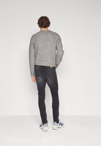 Suéter gris de canalé, jeans negros ajustados y zapatillas gris. El suéter tiene un cuello redondo y mangas largas, mostrando un diseño de punto texturizado.
