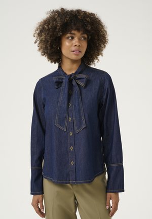 Donkerblauwe denimshirt met een strikjeskraag, lange mouwen, knoopsluiting aan de voorkant en contrasterende stiksels. Beschikt over een relaxte pasvorm en een gebogen zoom.