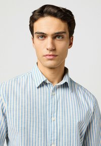 Camicia a righe blu chiaro e bianca con colletto button-down, realizzata in tessuto morbido, caratterizzata da una consistenza liscia e una leggera lucentezza.