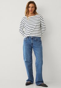 Gestreiftes Langarmhemd in Weiß und Marineblau, kombiniert mit hellblauen, ausgestellt geschnittenen Jeans. Flache schwarze Schuhe runden das Outfit ab.