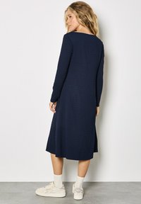 Vestido azul marino de manga larga con tejido texturizado, silueta en línea A y escote redondo. Combinado con zapatillas blancas y calcetines claros.