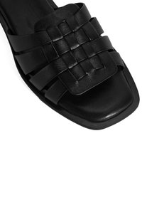 Sandal en cuir noir avec un design de bande tissée et un bout carré. Texture lisse avec une semelle plate et des accents minimaux.