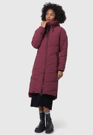 Doudoune bordeaux avec capuche, dotée d'une fermeture éclair sur toute sa longueur, de poches latérales et d'un design matelassé. Associée à une jupe noire à côtes et des bottes.