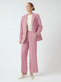 Lichtroze op maat gemaakt pak met een blazer met één knoop en wijde broekspijpen. De outfit heeft een crèmekleurige top en beige puntige hakken.