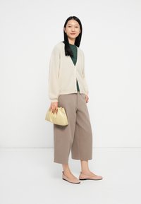 Cardigan bege claro, top verde escuro, calças largas bege, sapatilhas cor de rosa pálido, segurando uma mala de mão amarela suave. Texturas suaves e um ajuste descontraído.