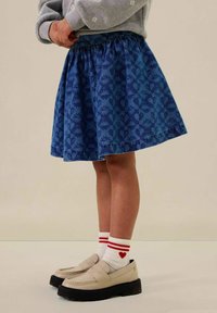 Jupe en denim bleu avec un motif floral, taille froncée, associée à des mocassins crème et des chaussettes blanches avec un cœur rouge et des rayures.