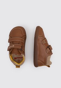 Chaussures en cuir marron avec deux bandes Velcro réglables, semelles en caoutchouc et doublure intérieure douce avec des accents jaunes. Détails de couture sur le côté visibles.