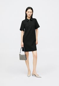 Juoda trumpomis rankovėmis suknelė su apykakle ir užtrauktuku priekyje, derinama su raštuotu rankiniu krepšeliu ir smėlio spalvos aukštakulniais. Vienodas, lygus faktūra.