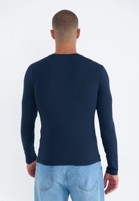 Langermet, tettsittende marineblå T-skjorte laget av mykt stoff. Har rund hals og glatt tekstur, kombinert med lyseblå jeans.