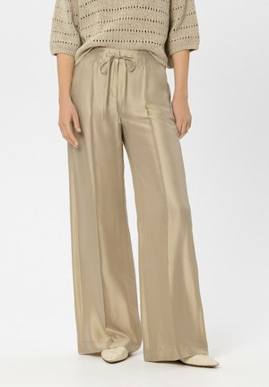 Beige wide-leg satin pants with drawstring waist worn with a light knitted sweater and cream pointed shoes on a white background.