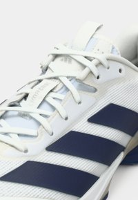 Chaussure de sport blanche avec des accents bleus, présentant une tige texturée, des lacets et trois bandes bleu foncé sur le côté. Design léger.
