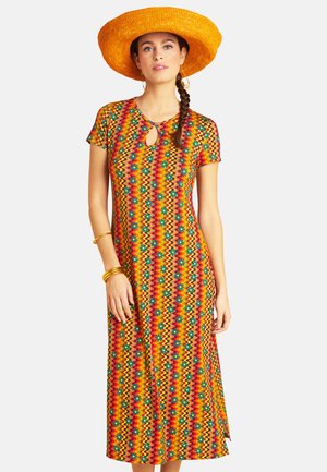 Frau trägt ein bunt gemustertes Midikleid mit kurzen Ärmeln, einem Ausschnitt mit Schlüsselloch, goldenen Armreifen und einen breitkrempigen orangefarbenen Strohhut.