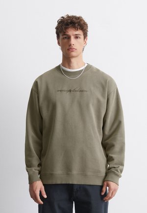 Olive green crewneck sweatshirt with ribbed cuffs and hem. Features embroidered text in a lighter shade across the chest. Soft fabric texture.