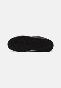 Semelle de chaussure de sport noire avec des motifs géométriques texturés et la marque "LACOSTE" visible sur la zone de la voûte plantaire.
