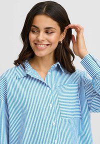 Blue and white striped button-up shirt with a chest pocket. The fabric is lightweight and features varied stripe widths for texture.