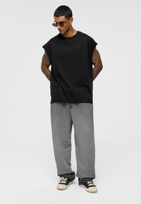 Zwarte katoenen mouwloze t-shirt gecombineerd met grijze sweatpants van zacht materiaal; heeft zwarte sneakers met crèmekleurige accenten.