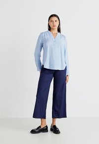 Camisa de rayas azul claro con cuello, combinada con pantalones de pierna ancha en azul marino oscuro y mocasines negros. Tejido suave, corte relajado.