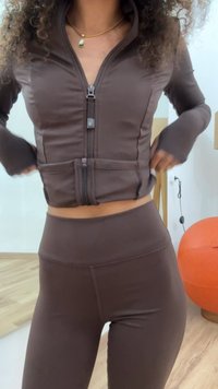 Giacca sportiva marrone con zip, dal design aderente, maniche lunghe e aperture per il pollice, abbinata a leggings a vita alta coordinati.