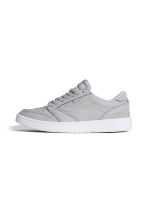 Lage grijze Vans sneaker met witte zool, veters aan de voorkant en een subtiel golvend stiksel detail aan de zijkant op een effen witte achtergrond.