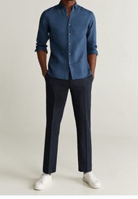 Niebieska koszula na guziki z długimi rękawami, zestawiona z ciemnymi spodniami w paski i białymi trampkami. Koszula ma klasyczny kołnierzyk i gładką teksturę.