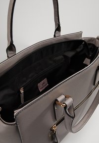 Sac à main structuré gris avec doublure intérieure noire, doubles poignées, poche avant zippée et compartiment intérieur zippé avec étiquette de marque.