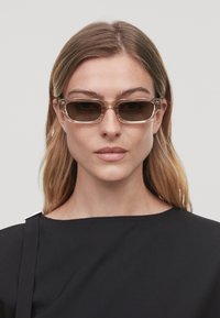 Lunettes de soleil avec une monture transparente, des verres teintés foncés, un design rectangulaire et des côtés épais, complétant un haut noir au design simple.