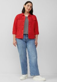 Helle rote Jeansjacke über einem schwarz-weißen gestreiften Shirt, kombiniert mit blauen weiten Jeans und weißen Plateausneakern.