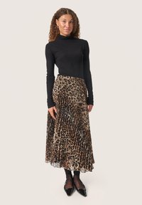 Sort langærmet top parret med en plisseret maxi-nederdel i leopardmønster lavet af et letvægtsstof. Sorte spidse sko afslutter looket.