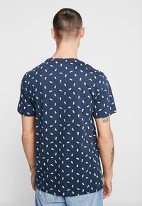 Camiseta de algodón azul marino con mangas cortas, con un patrón disperso de piñas blancas por todo el tejido. Cuello plano, corte casual.