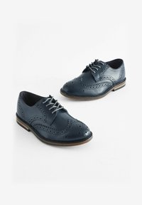 Marineblå læder snøresko med perforerede brogue-detaljer, rund tå og en kontrasterende brun sål. Standard bredde design.