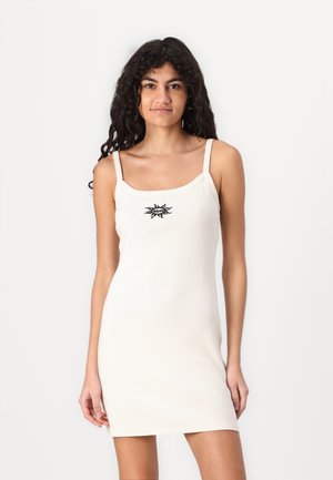 Knit white mini dress with adjustable spaghetti straps and a black sunburst logo centered on the chest. Smooth texture, body-hugging fit.