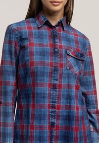 Niebiesko-czerwona koszula w kratę wykonana z bawełny. Posiada zapięcie na guziki, kieszeń na piersi oraz usztywniony kołnierzyk o gładkiej fakturze.