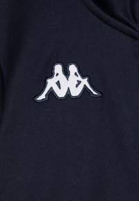 Tamsiai mėlynas audinys su baltais siuvinėtais logotipais, kuriuose pavaizduoti du sėdintys asmenys. Tekstūra yra rypuota, o paviršius lygus.
