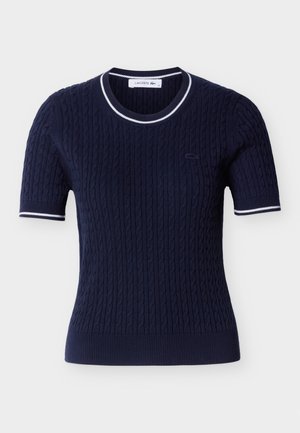 Tengerészkék, rövid ujjú kötött felső kábelmintával, fehér csíkos szegéllyel a galléron és az ujj szélén, valamint kis hímzett logóval a mellrészen.