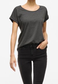 Ciemnoszary t-shirt z krótkim rękawem wykonany z miękkiej tkaniny, o luźnym kroju, z podwiniętymi rękawami i okrągłym dekoltem, w parze z czarnymi obcisłymi dżinsami.