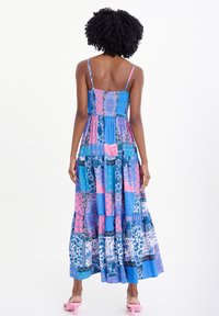 Maxi šaty s multikolorovým patchwork designem v modré a růžové barvě, s tenkými nastavitelnými ramínky a volánkovou sukní. Růžové sandály na podpatku.