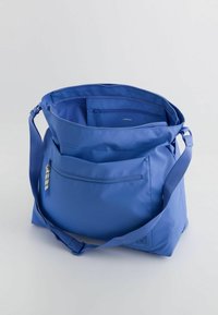 Blue nylon shoulder bag with a zip closure, adjustable strap, and front pocket. Interior features additional compartments for organization.