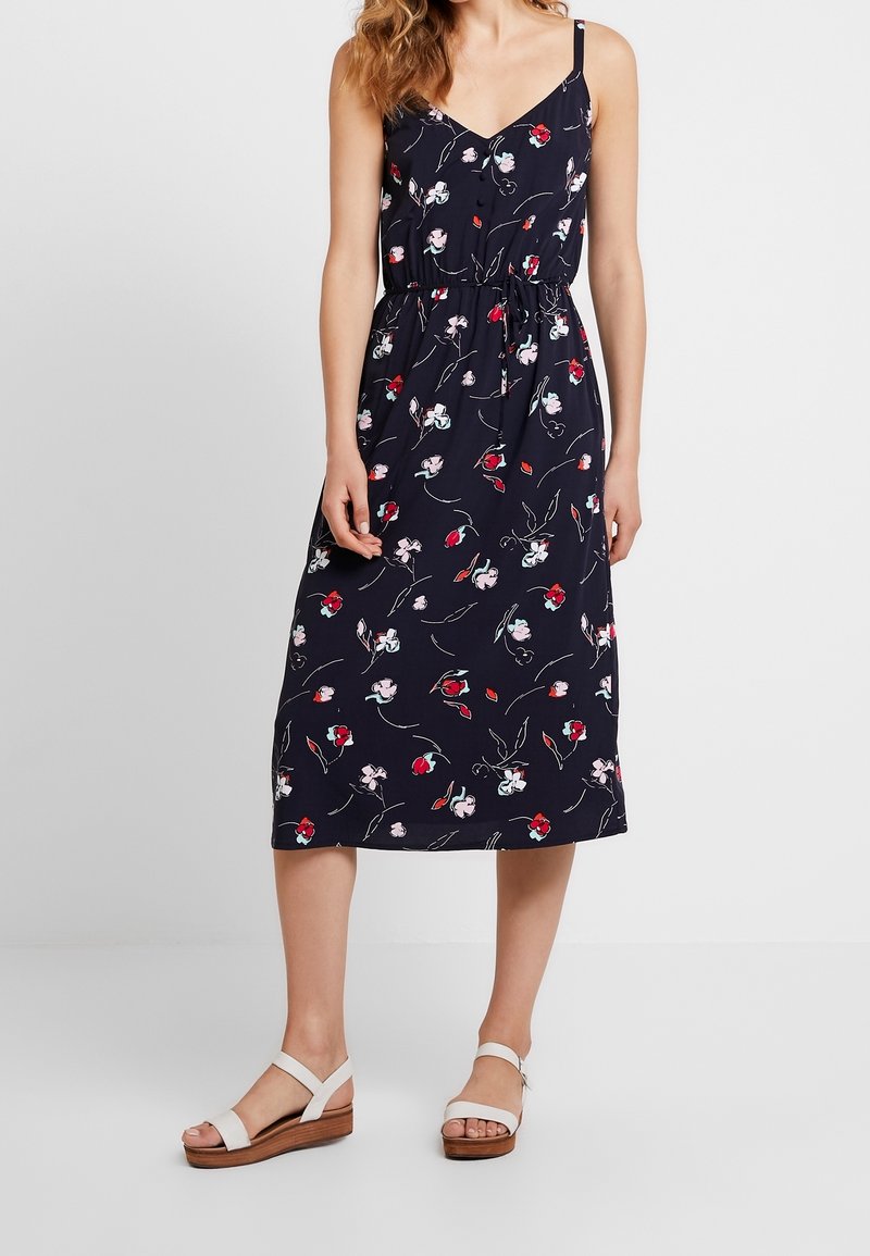 Robe fleurie bleu marine avec des bretelles fines, taille à cordon et longueur midi. Présente des motifs de fleurs rouges et roses sur un tissu doux.