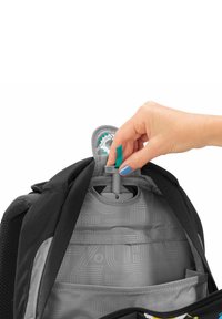 Schwarzer Rucksack mit grauem Innenfach. Eine Hand justiert ein grau-grünes Metallteil, das geometrische Muster im Futter aufweist.