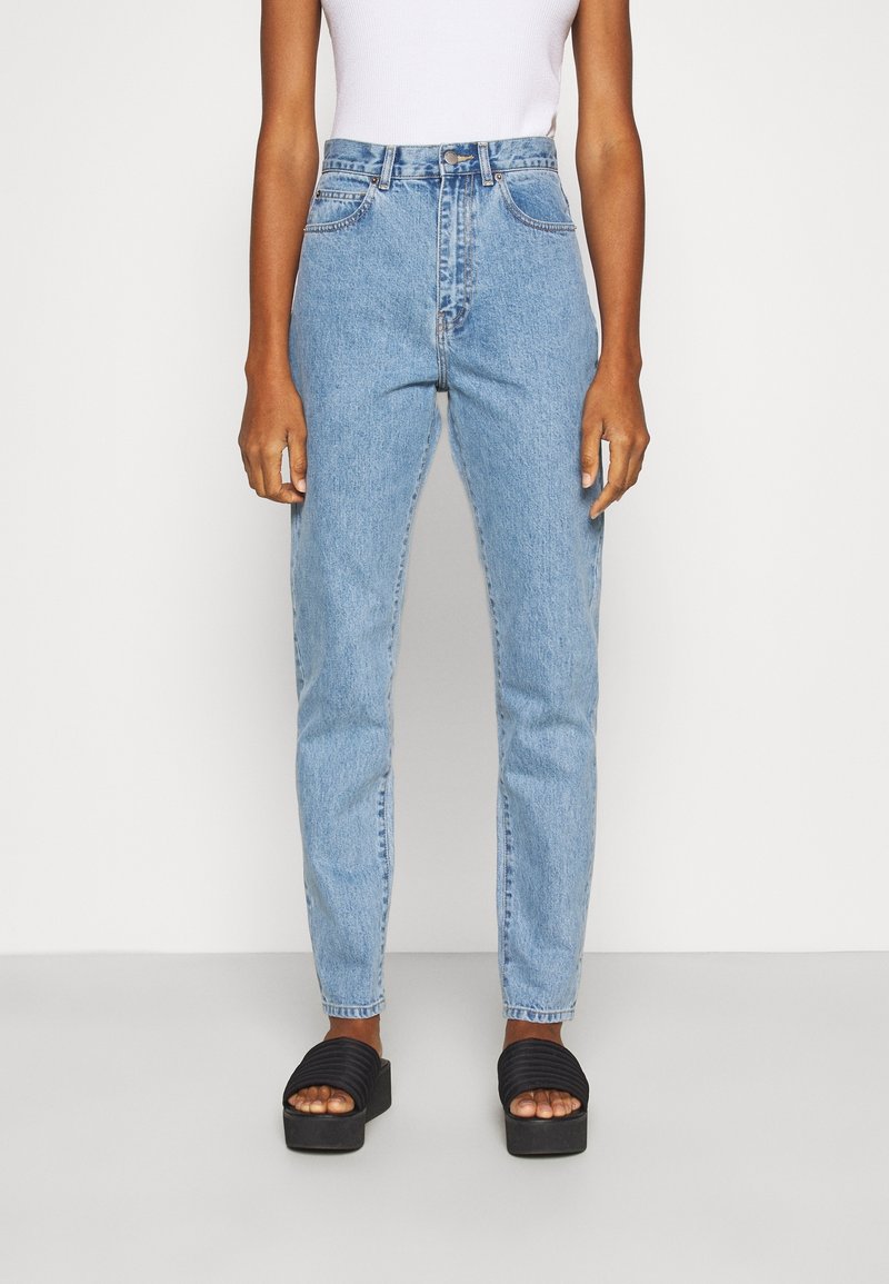 Světle modré džíny s vysokým pasem a rovnými nohavicemi, s předním zipem a knoflíkem, kombinované s černými platformovými sandály.