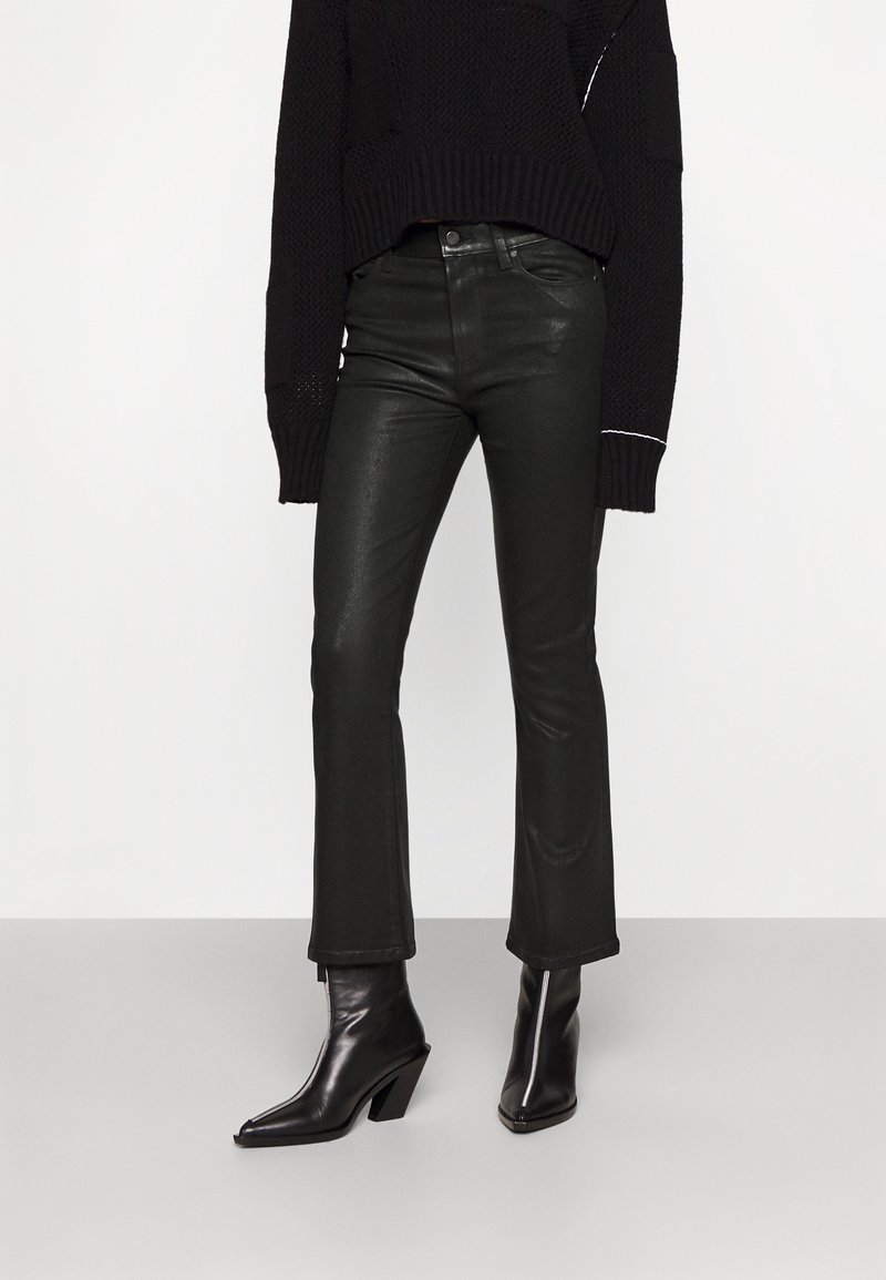 Jeans de imitación cuero negros acampanados con cintura alta y un ligero brillo, combinados con botas negras hasta el tobillo con tacón ancho.