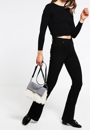 Šedá a bílá kabelka s texturovaným kožíškem v dolní části a plochou, filcovou klopou. Černý ramenní popruh; zobrazeno s černým outfitem.