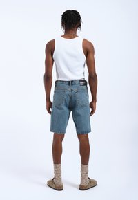 Shorts in denim di colore azzurro chiaro con una vestibilità rilassata, dotati di un'etichetta sulla cintura posteriore. Abbinati a una canotta bianca e scarpe slip-on beige con calze testurizzate.