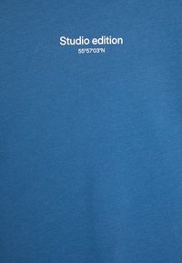 Modrá bavlnená tričko s bielym textom "Studio edition" a súradnicami "55°57'03''N." Hladká textúra, okrúhly výstrih, ležérny dizajn.