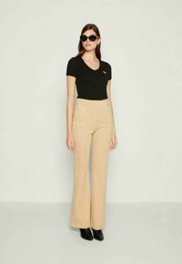 Camiseta negra ajustada con cuello en V, pantalones beige de pierna ancha y gafas de sol negras. Texturas suaves, corte a medida y diseño minimalista.
