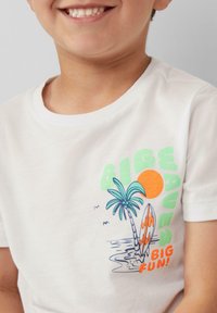Biała bawełniana koszulka z kolorową grafiką słońca, palm i deski surfingowej z napisem "WIELKA FALA WIELKA ZABAWA!" w różnych kolorach.